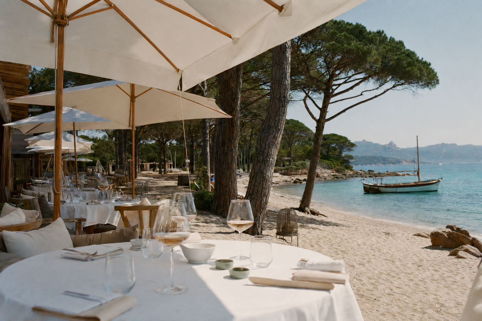A Corsican beach club with white parasols, pine trees and turquoise water, late morning