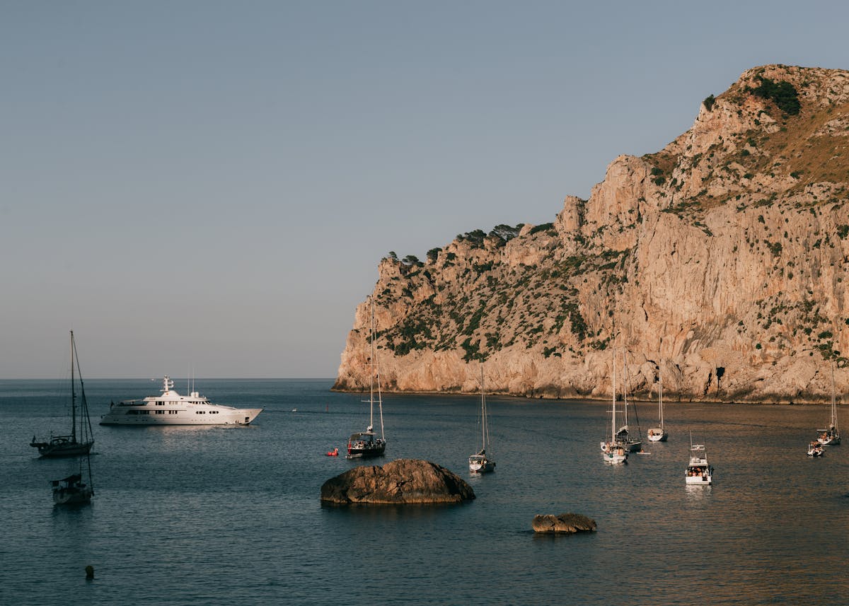 Sailing yacht against a backdrop of dramatic mountainous coastline