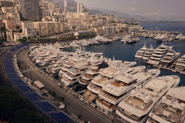 Yachts moored stern-to-stern along the quay in Port Hercule, Monaco, with grandstands rising behind them
