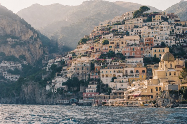 Pastel houses stacked up the cliffside above Positano harbour, photographed from a boat in soft morning light