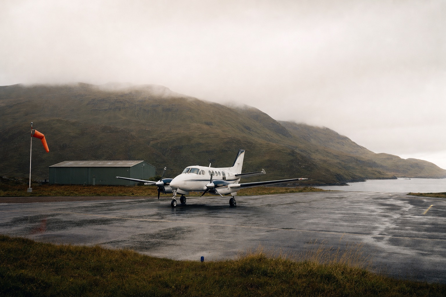 A light turboprop parked on the short asphalt strip at Broadford on the Isle of Skye, with green hills behind and low cloud over the Sound of Sleat
