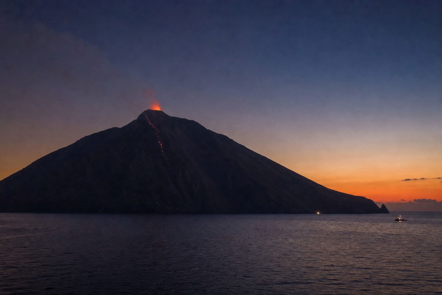 Stromboli volcano silhouetted at dusk with an orange glow at its crater