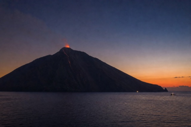 Stromboli volcano silhouetted at dusk with an orange glow at its crater
